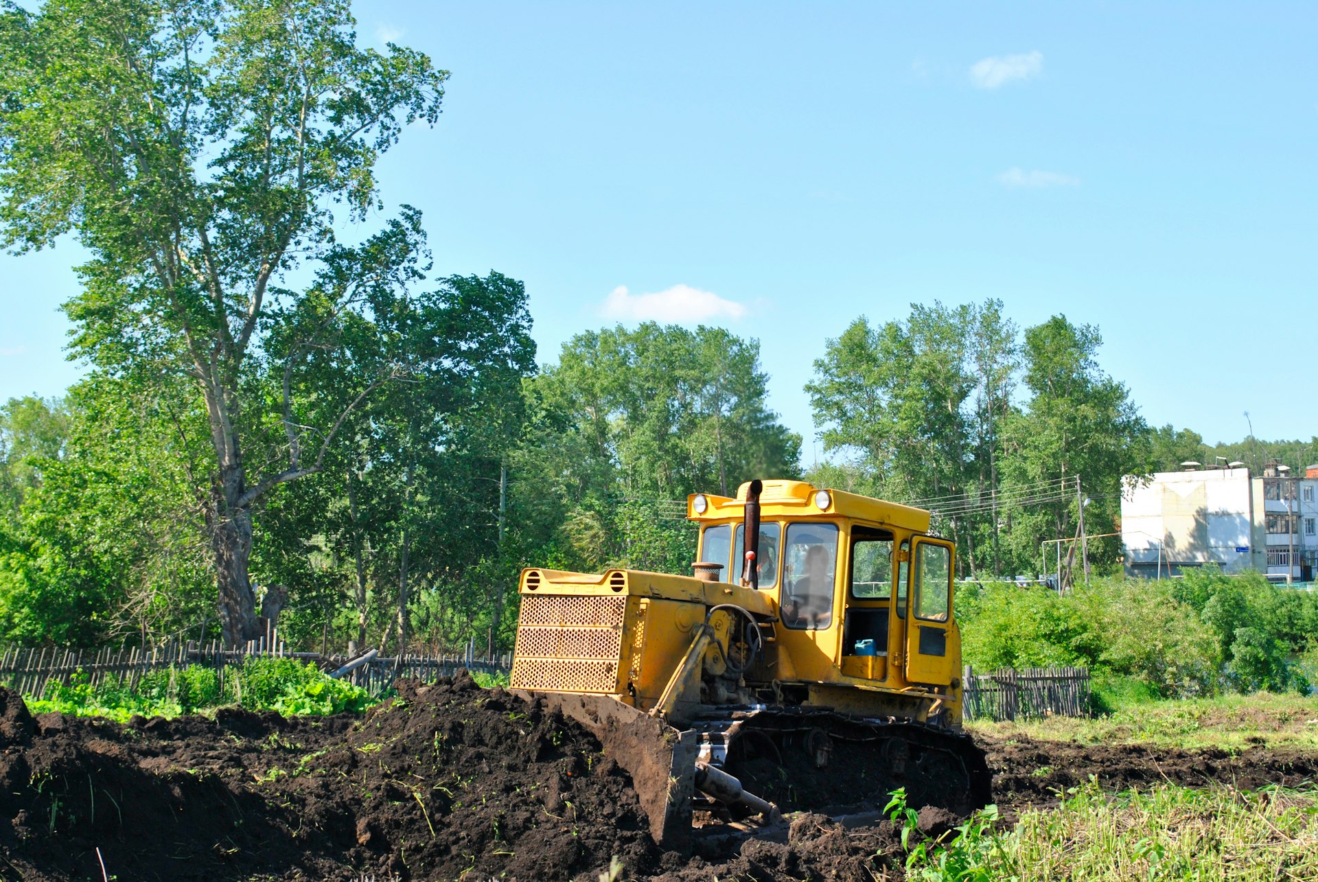 a bulldozer digging through a field with trees in the background